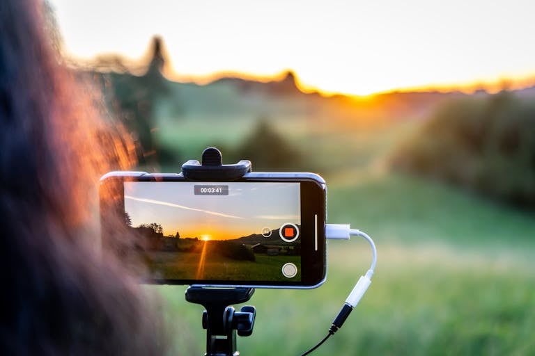 A smartphone recording a beautiful sunset in a lush green landscape.